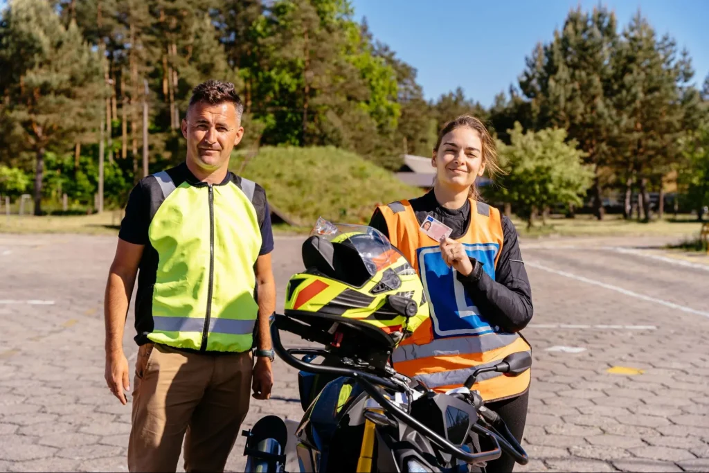 młoda kobieta z prawem jazdy w ręku stojąca z instruktorem przy motocyklu